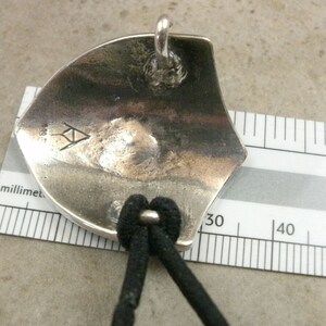 Pu&ograve; includere: Ciondolo in argento con un design triangolare e l'iscrizione "999" sul retro. Il ciondolo &egrave; attaccato a un cordino nero.