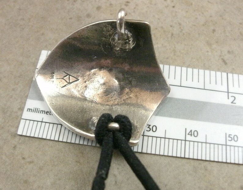 Pu&ograve; includere: Ciondolo in argento con un design triangolare e l'iscrizione "999" sul retro. Il ciondolo &egrave; attaccato a un cordino nero.