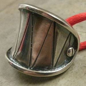 May include: A silver ring with a textured, geometric design. The ring is curved and has a small, round bead on the side.