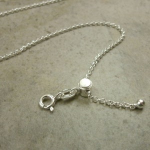 May include: A silver chain necklace with a sliding clasp and a small ball at the end.
