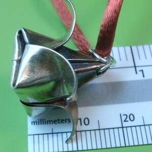 May include: A silver origami flower pendant with a red ribbon attached. The pendant is about 10 millimeters in diameter.