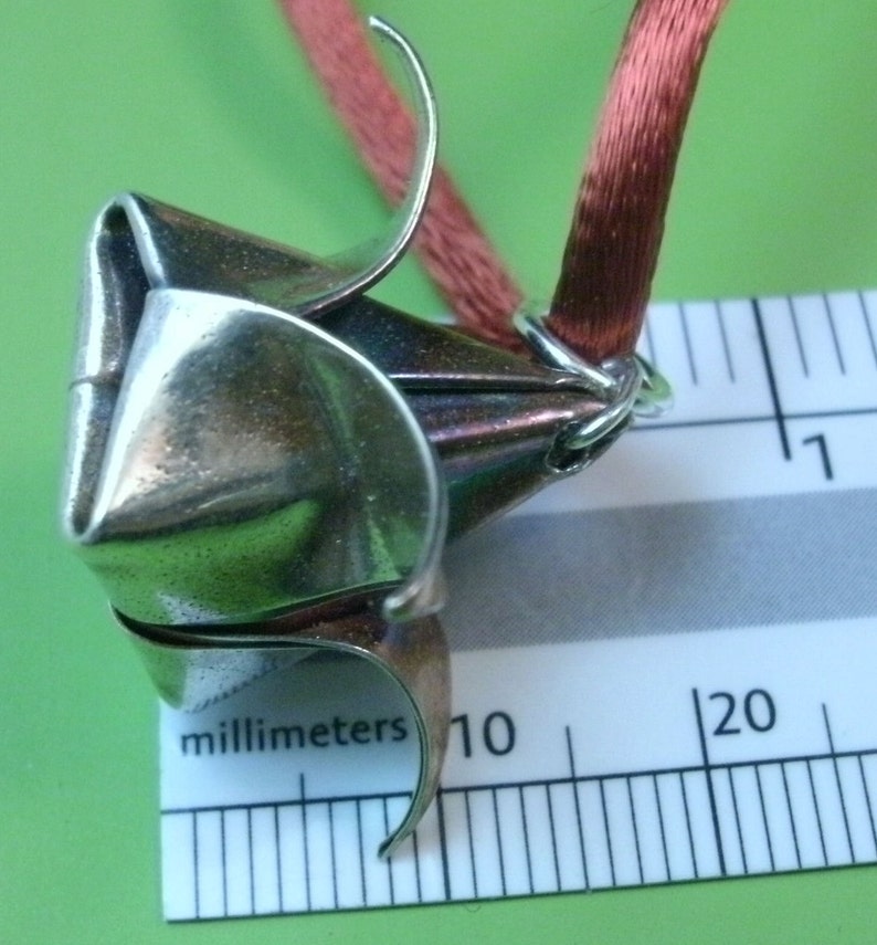 May include: A silver origami flower pendant with a red ribbon attached. The pendant is about 10 millimeters in diameter.