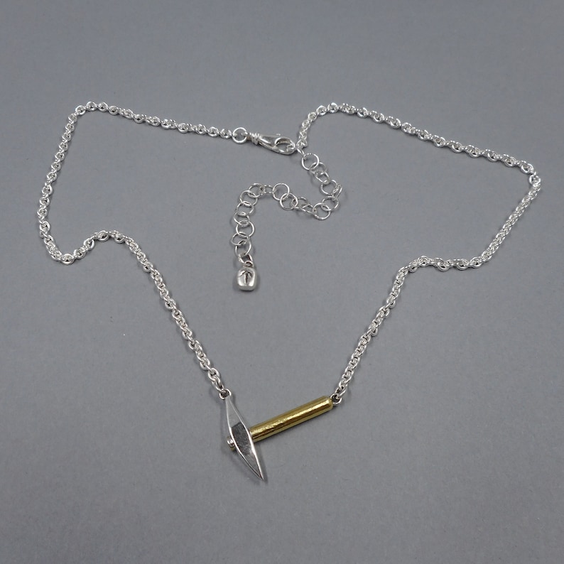 May include: A silver chain necklace with a silver and gold pickaxe pendant.