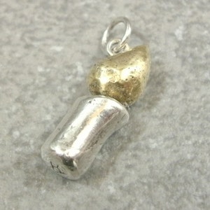 May include: A silver and gold charm in the shape of a candle. The candle is made of two pieces, the base is silver and the flame is gold.