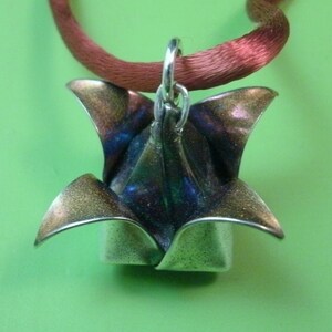 May include: A silver origami flower pendant with a blue and purple iridescent finish, hanging from a red satin ribbon.