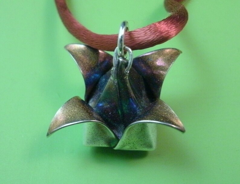 May include: A silver origami flower pendant with a blue and purple iridescent finish, hanging from a red satin ribbon.
