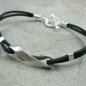 May include: A black leather bracelet with a silver clasp and a silver twisted design.