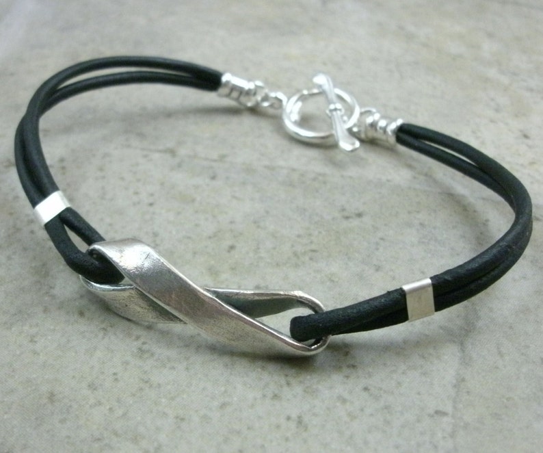 May include: A black leather bracelet with a silver clasp and a silver twisted design.