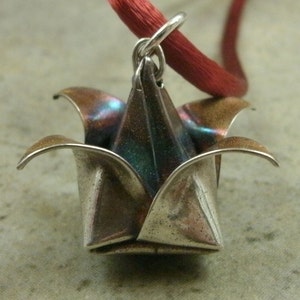 May include: A silver origami flower pendant with a red cord. The flower has a metallic sheen and is folded into a delicate shape.