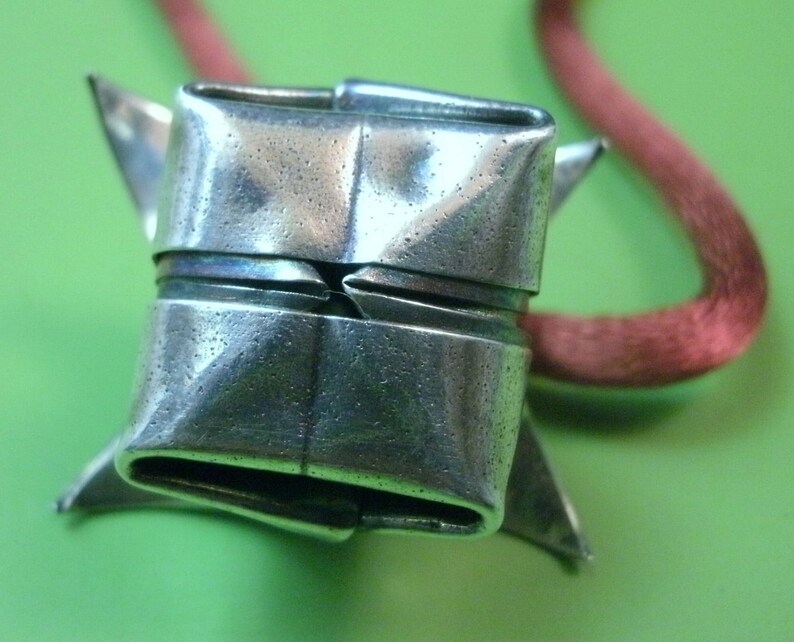 May include: A silver origami-style pendant with a folded design, hanging from a red cord.