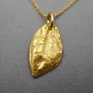 以下が含まれることがあります： 金の葉のペンダントネックレス。葉は葉脈と質感のある表面で詳細に描かれています。