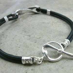 May include: A black leather bracelet with a silver toggle clasp. The clasp is shaped like a golf club.