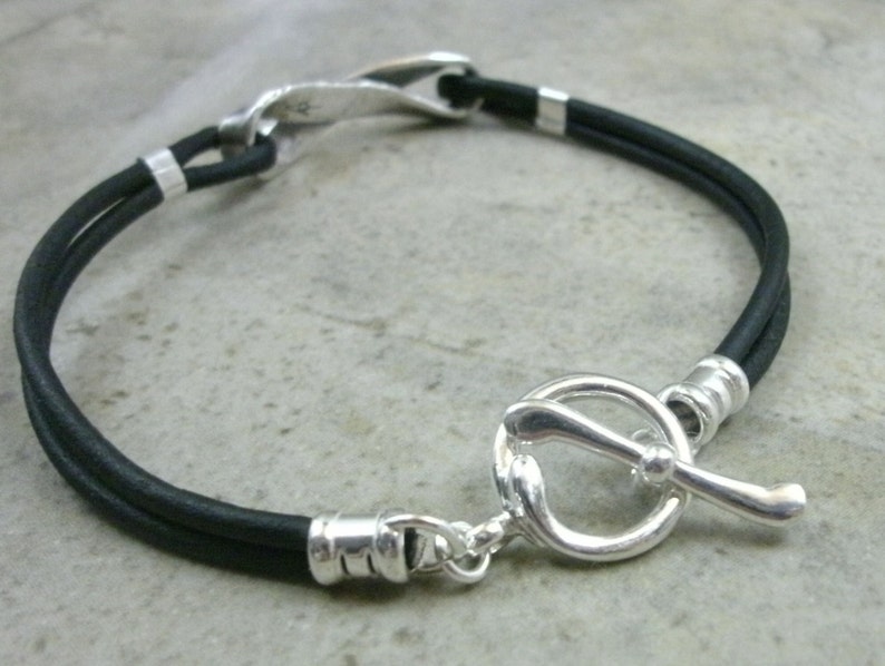 May include: A black leather bracelet with a silver toggle clasp. The clasp is shaped like a golf club.