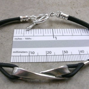 May include: A black leather bracelet with a silver twisted bar clasp. The bracelet is 3.8 cm long.