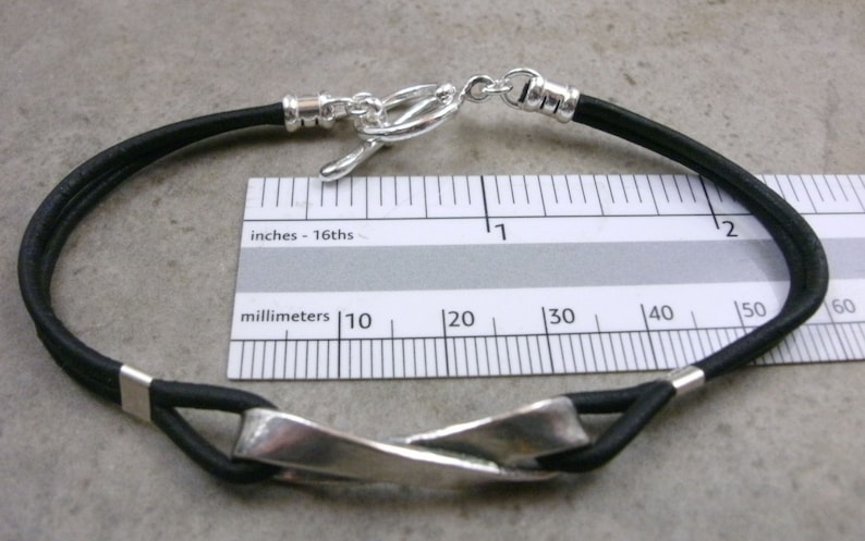 May include: A black leather bracelet with a silver twisted bar clasp. The bracelet is 3.8 cm long.