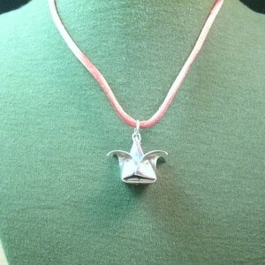May include: A silver origami flower pendant on a pink cord necklace.