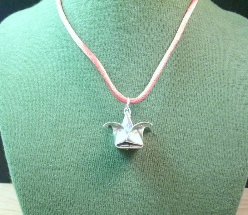 May include: A silver origami flower pendant on a pink cord necklace.