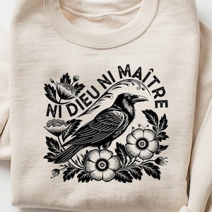 Puede incluir: Sudadera color crema con un gr&aacute;fico en blanco y negro de un cuervo rodeado de flores, con el texto "Ni Dieu Ni Ma&icirc;tre". La parte superior de manga larga est&aacute; hecha de un material suave.