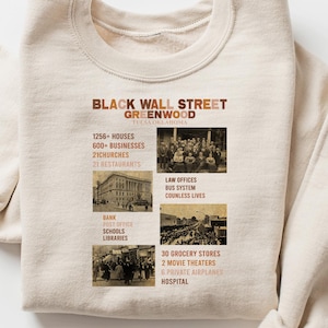 May include: Cream-colored sweatshirt with the text "Black Wall Street Greenwood" and historical facts. The design includes images and text about houses, businesses, churches, law offices, and more. A comfortable, long-sleeved top.