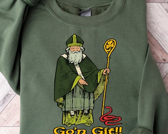May include: Military green sweatshirt featuring a graphic of a saintly figure in green robes, holding a gold staff. The text "Go'n Git!!" is printed in yellow. The sweatshirt has long sleeves with ribbed cuffs.