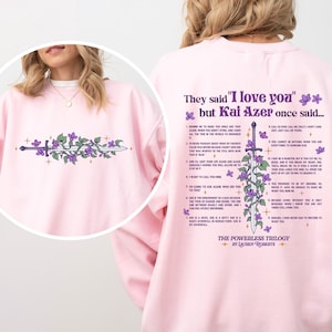 May include: A light pink sweatshirt with a floral and sword design on the front and back. The back features text that reads "They said 'I love you' but Kai Azer once said..." and a list of quotes. The sweatshirt is part of "The Powerless Trilogy."