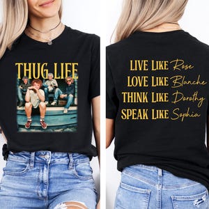 May include: Black t-shirt with a graphic of a group of people and the words "THUG LIFE" in yellow. The back of the shirt has the words "LIVE LIKE Rose, LOVE LIKE Blanche, THINK LIKE Dorothy, SPEAK LIKE Sophia" in yellow.