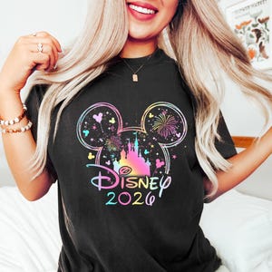 May include: Black t-shirt featuring a colorful Disney design. The design includes a Mickey Mouse head outline with fireworks, a castle, and the word "Disney" with the year "2026" in a rainbow gradient.