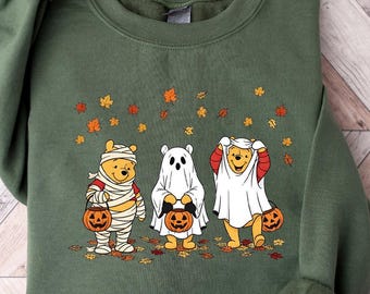 May include: An olive green sweatshirt with a Halloween design. The graphic shows three cartoon bears in Halloween costumes: a mummy, a ghost, and a character in a sheet, each with a pumpkin. There are autumn leaves above the characters.