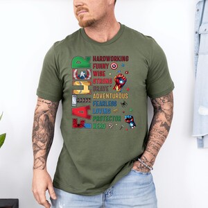 May include: Olive green t-shirt with the word "FATHER" in colorful block letters. The shirt features a list of positive attributes like "hardworking," "funny," and "hero" in a superhero theme.