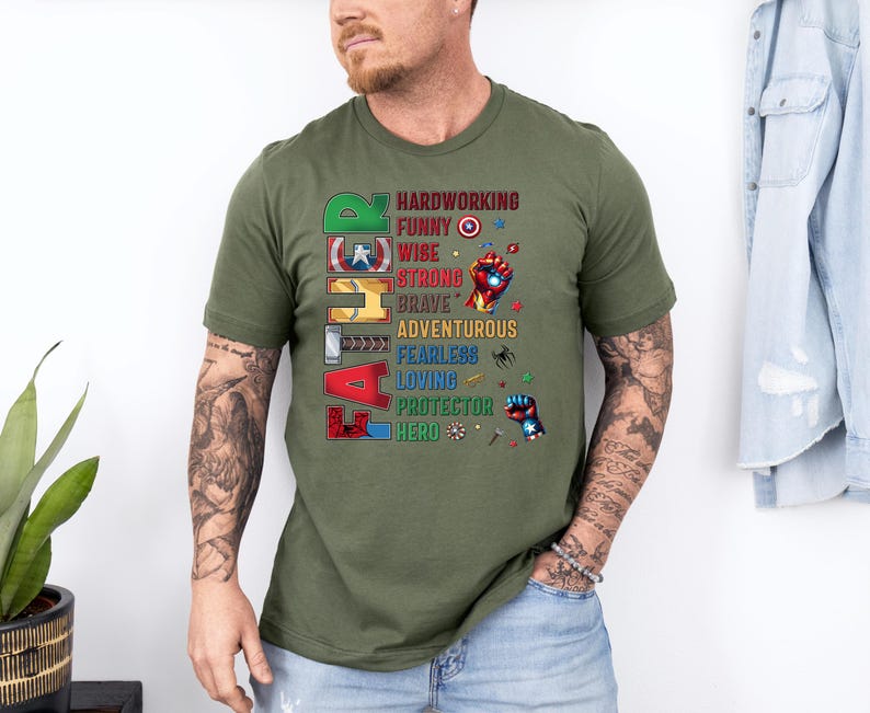 May include: Olive green t-shirt with the word "FATHER" in colorful block letters. The shirt features a list of positive attributes like "hardworking," "funny," and "hero" in a superhero theme.