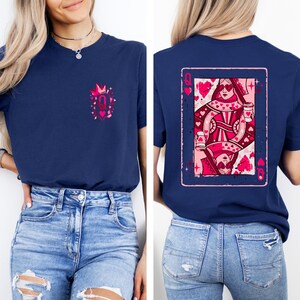 May include: Navy blue t-shirt featuring a pink and red Queen of Hearts playing card design on the back. The front of the shirt has a small pink graphic with a crown and the letter "Q". The shirt is paired with blue jeans.
