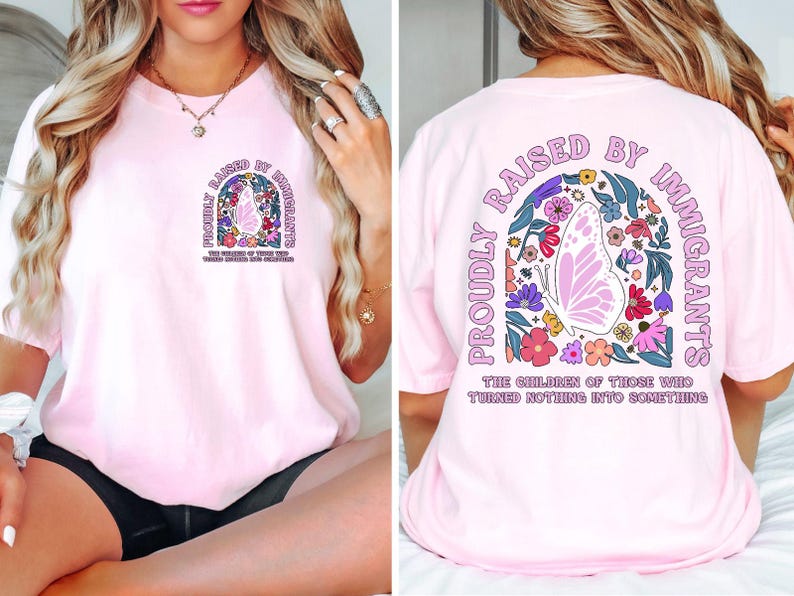 May include: Light pink t-shirt with a graphic on the front and back. The front graphic says "Proudly Raised by Immigrants" with a butterfly and floral design. The back graphic repeats the text and design. The text on the shirt says "The children of those who turned nothing into something."