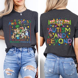 K&ouml;nnte beinhalten: Dunkelgraues T-Shirt mit einer farbenfrohen Grafik zur F&ouml;rderung des Autismus-Bewusstseins. Auf der Vorderseite stehen die Worte "Autismus Awareness and beyond" mit Zeichentrickfiguren. Auf der R&uuml;ckseite steht "Autism and Beyond" mit einer Rakete und Puzzleteilen.