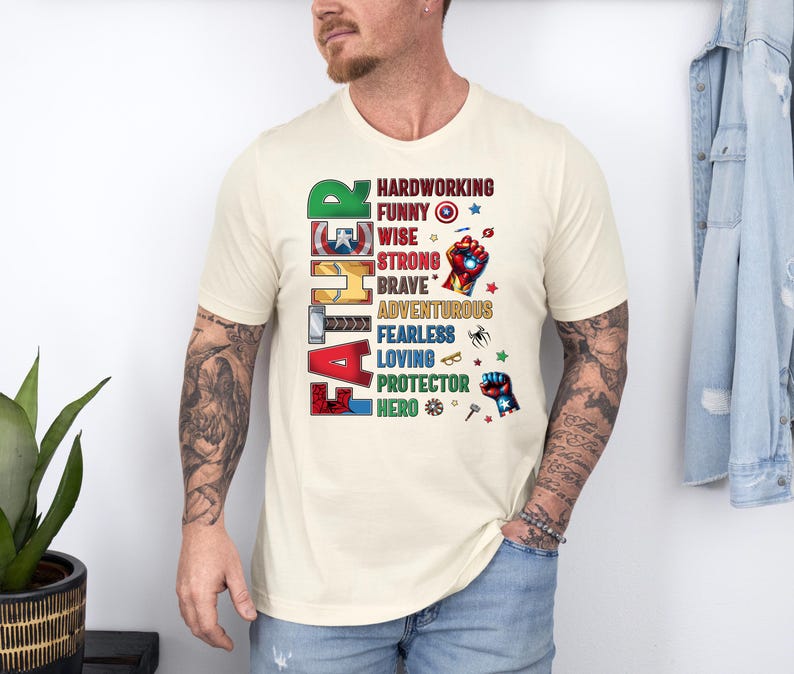 May include: Cream-colored t-shirt with the word "FATHER" vertically down the left side in colorful, comic-book style lettering. The shirt features a list of positive attributes like "hardworking" and "hero" in a matching font.