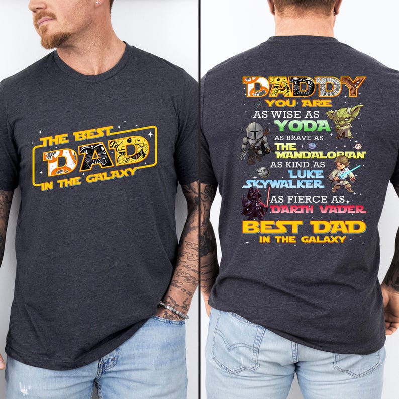Puede incluir: Camiseta gris oscuro con el texto "THE BEST DAD IN THE GALAXY" en amarillo y naranja. La parte trasera de la camiseta tiene el texto "DADDY" y varios personajes de Star Wars, incluyendo a Yoda y Darth Vader.