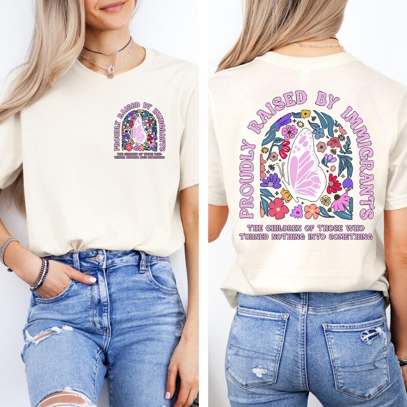 May include: Cream-colored t-shirt with a butterfly and floral design. The front and back of the shirt feature the text "PROUDLY RAISED BY IMMIGRANTS" in a curved arch, with additional text below.