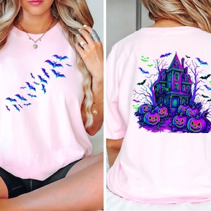 May include: Light pink t-shirt featuring a Halloween theme. The front displays a flock of blue and purple bats. The back showcases a haunted house, pumpkins, bats, and trees in vibrant colors. A festive and spooky design.