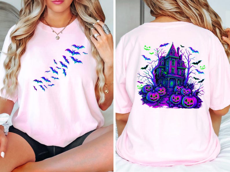 May include: Light pink t-shirt featuring a Halloween theme. The front displays a flock of blue and purple bats. The back showcases a haunted house, pumpkins, bats, and trees in vibrant colors. A festive and spooky design.