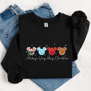 May include: Black crewneck sweatshirt featuring a festive design with Mickey Mouse-themed Christmas ornaments. The ornaments include candy canes, snowflakes, and gingerbread. The text "Mickey's Very Merry Christmas" is written in cursive.