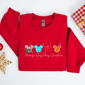May include: A red sweatshirt with a festive design featuring Mickey Mouse-themed Christmas elements. The design includes candy canes, snowflakes, and Mickey Mouse heads in various colors. The text "Mickey's Very Merry Christmas" is written in script.
