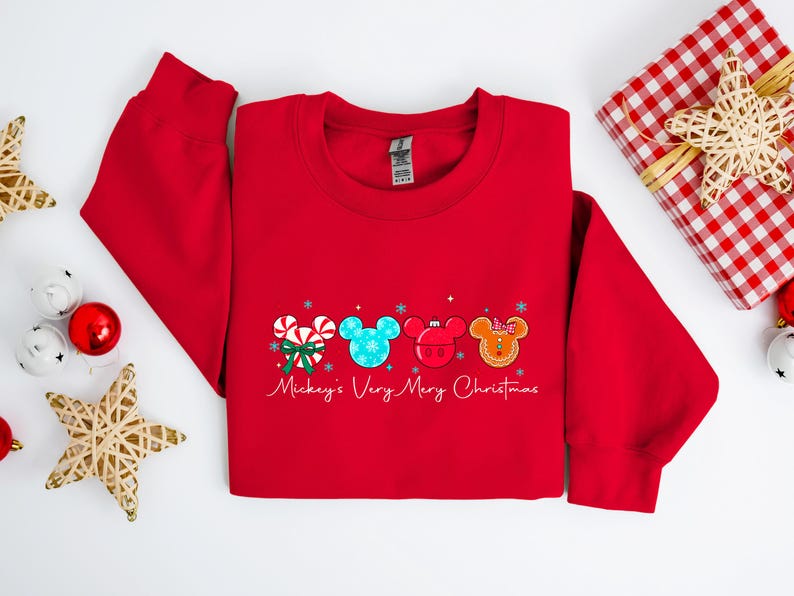 May include: A red sweatshirt with a festive design featuring Mickey Mouse-themed Christmas elements. The design includes candy canes, snowflakes, and Mickey Mouse heads in various colors. The text "Mickey's Very Merry Christmas" is written in script.