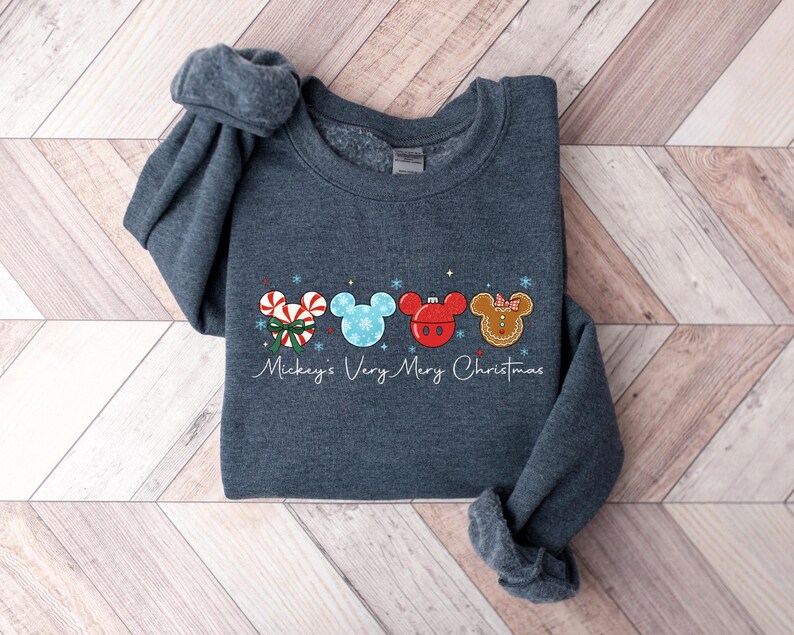 May include: A dark gray sweatshirt featuring a festive design with four Mickey Mouse-shaped ornaments. The ornaments include a candy cane, snowflake, red ornament, and gingerbread cookie. The text "Mickey's Very Merry Christmas" is written below the ornaments.