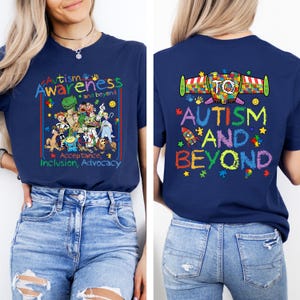 K&ouml;nnte beinhalten: Marineblaues T-Shirt mit den Worten "Autismus-Bewusstsein und dar&uuml;ber hinaus" in farbenfrohem Text. Die Vorderseite des Shirts zeigt eine Cartoon-Illustration verschiedener Charaktere. Auf der R&uuml;ckseite des Shirts stehen die Worte "Autismus und dar&uuml;ber hinaus" mit einer Raketen-Grafik.