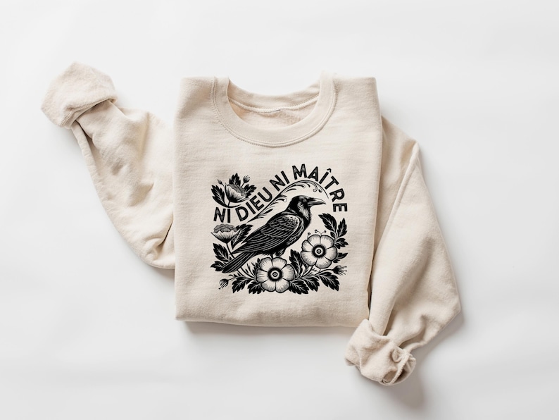 Puede incluir: Sudadera color crema con un gr&aacute;fico en blanco y negro de un cuervo rodeado de flores, con el texto "Ni Dieu Ni Ma&icirc;tre". La parte superior de manga larga est&aacute; hecha de un material suave.