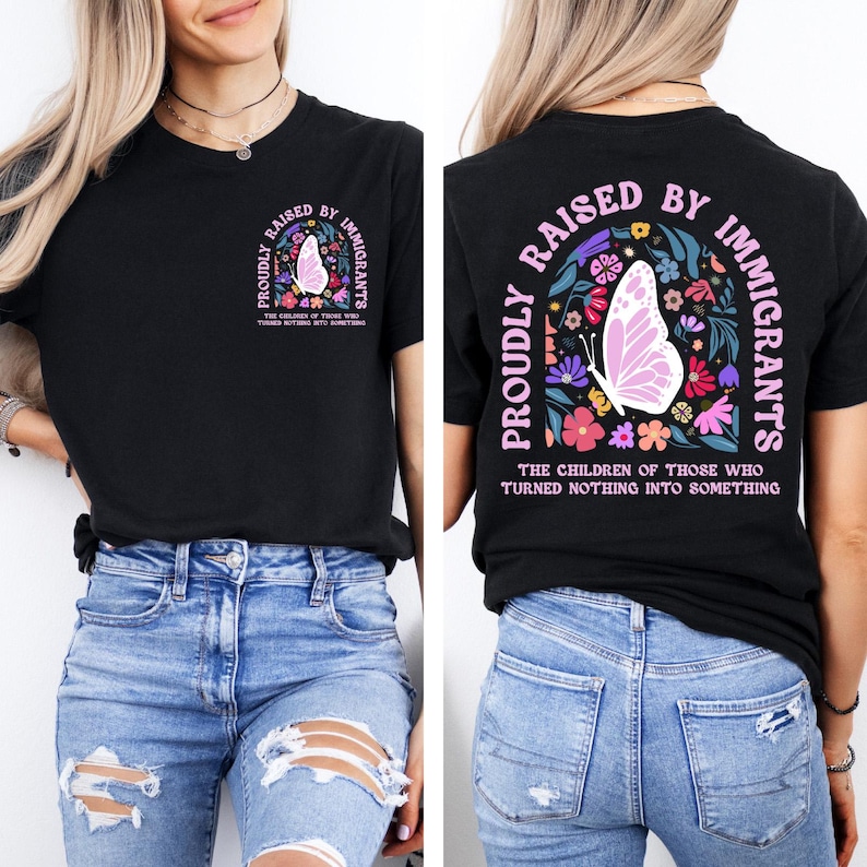 May include: Black t-shirt with the text "PROUDLY RAISED BY IMMIGRANTS" in white and pink. The design includes a butterfly and floral elements. The phrase "THE CHILDREN OF THOSE WHO TURNED NOTHING INTO SOMETHING" is also printed on the shirt.