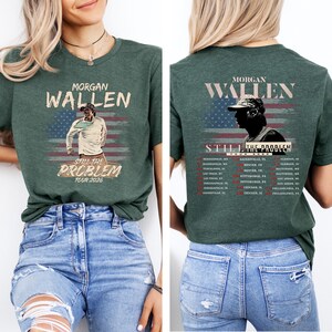 Może przedstawiać: Ciemnozielona koszulka z napisem "MORGAN WALLEN" nad wizerunkiem osoby na tle amerykańskiej flagi. Pod obrazem znajduje się napis "STILL THE PROBLEM TOUR 2026". Z tyłu koszulki znajduje się r&oacute;wnież napis "MORGAN WALLEN" oraz lista miejsc koncert&oacute;w.