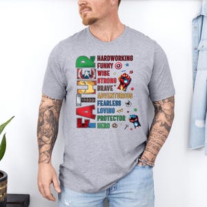 May include: A gray t-shirt with the word "FATHER" in colorful block letters. The shirt features a list of positive attributes like "hardworking," "funny," and "hero," with superhero-themed graphics.