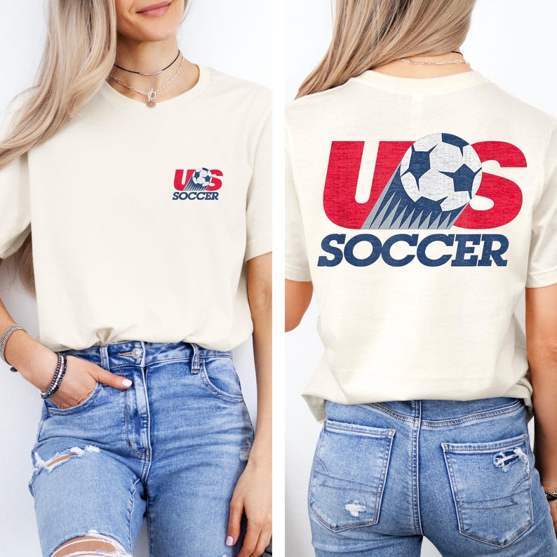Puede incluir: Una camiseta de manga corta color crema con un peque&ntilde;o gr&aacute;fico en el pecho izquierdo que dice US SOCCER con un bal&oacute;n de f&uacute;tbol. La parte posterior de la camiseta muestra un gran gr&aacute;fico rojo US con un bal&oacute;n y la palabra SOCCER en azul.