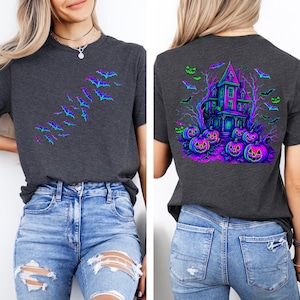 May include: Dark gray t-shirt featuring a Halloween design. The front displays a flock of bats in shades of blue and purple. The back showcases a haunted house, pumpkins, and bats in vibrant neon colors, perfect for the spooky season.