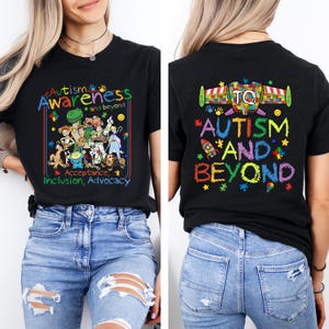 K&ouml;nnte beinhalten: Schwarzes T-Shirt mit den Worten "Autismus-Bewusstsein und dar&uuml;ber hinaus" in farbenfrohem Text. Auf der Vorderseite des Shirts sind Zeichentrickfiguren und die Worte "Akzeptanz, Inklusion, Advocacy" zu sehen. Auf der R&uuml;ckseite des Shirts steht "Autismus und dar&uuml;ber hinaus".